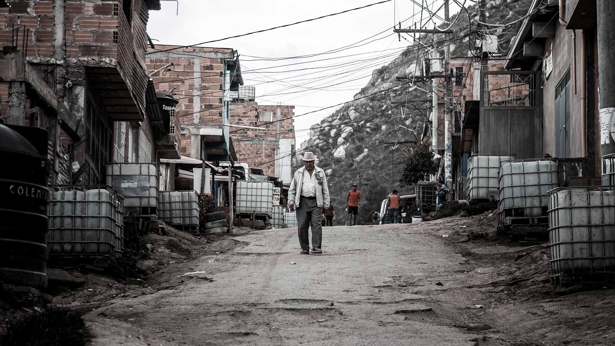 A man in a cowboy hat walking down a street with makeshift dwellings